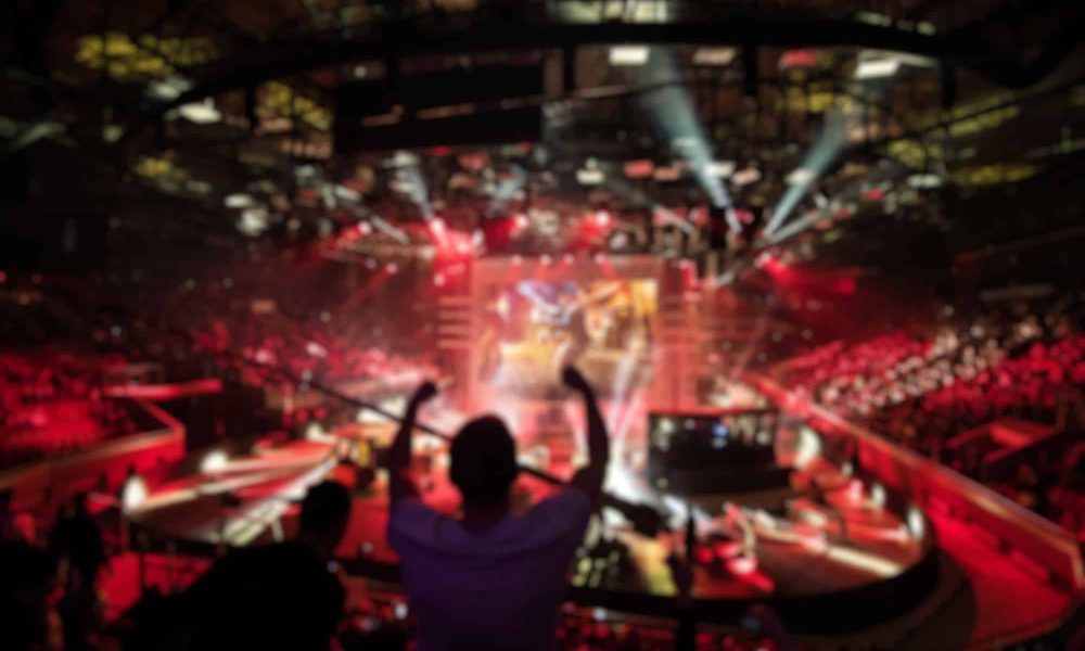 Abstract blurred background of big esports gaming event at big arena. Man with a hands raised
