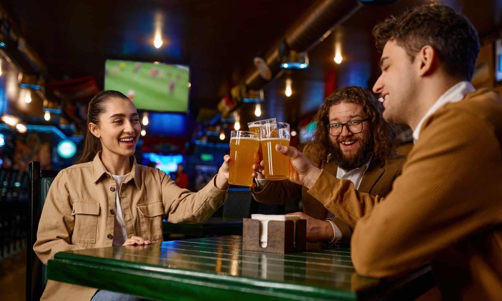 Friends watching football match clinking beer mug rest in sport bar